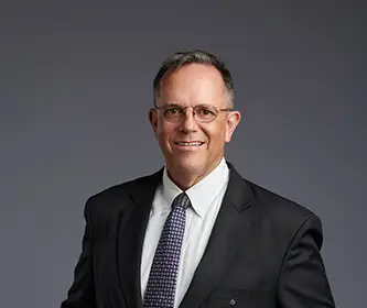 A Picture of man Standing in front of grey background wall and smiling.
